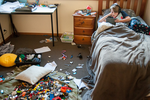 Child laying in bed on electronic device with a very messy room
