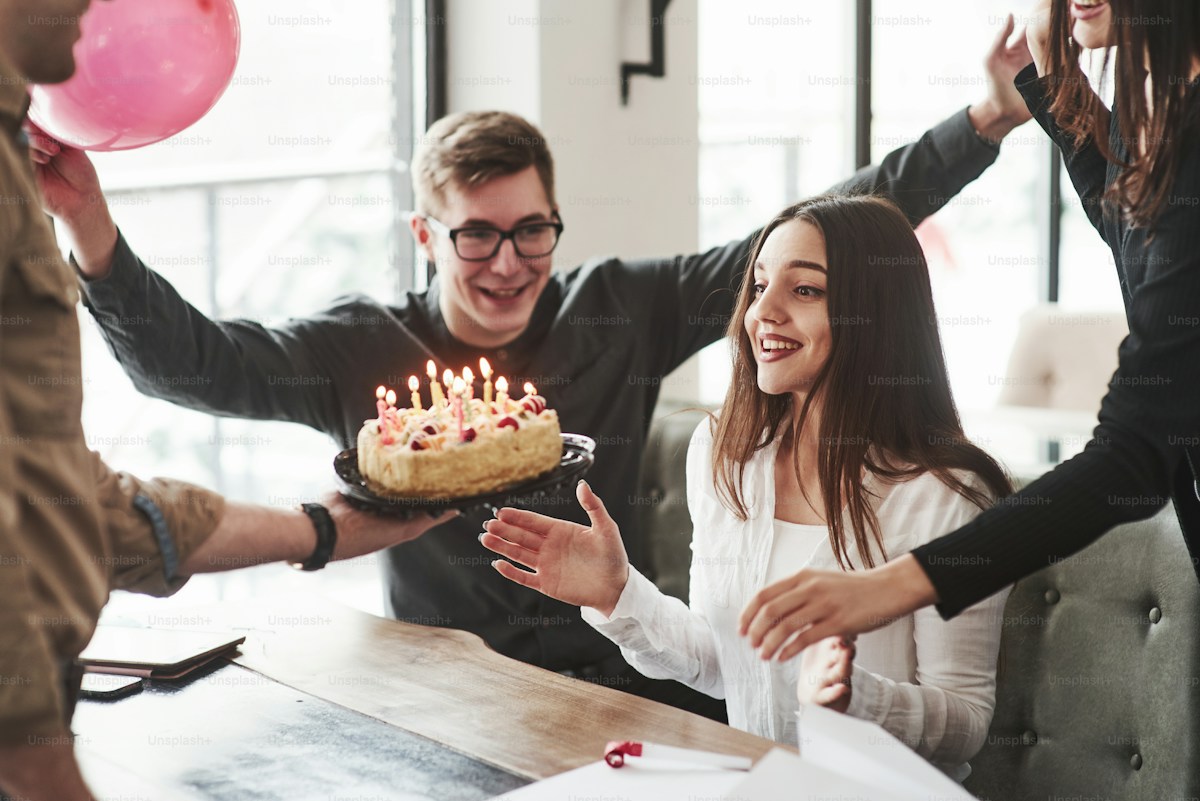 Friendly coworkers surprising colleague on her birthday with cake and celebration