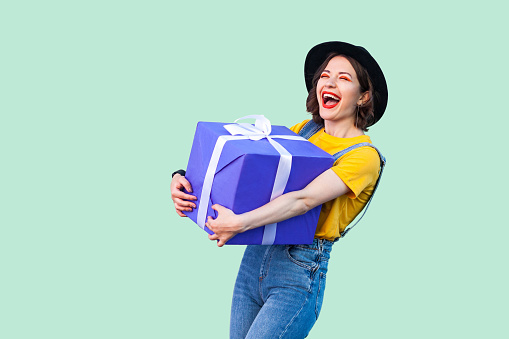 Satisfied happy young girl holding big gift box with toothy smile and laughing