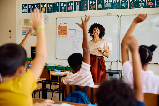 Elementary school teacher smiling and asking questions with children hands raised